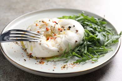 Photo of Delicious burrata cheese, arugula and spices on grey table, closeup