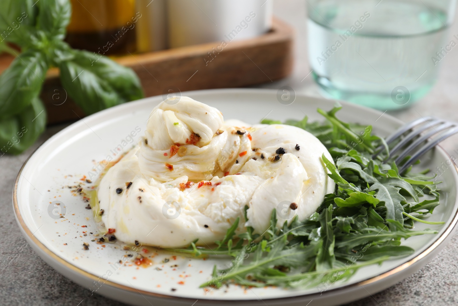 Photo of Delicious burrata cheese, arugula and spices on grey table, closeup