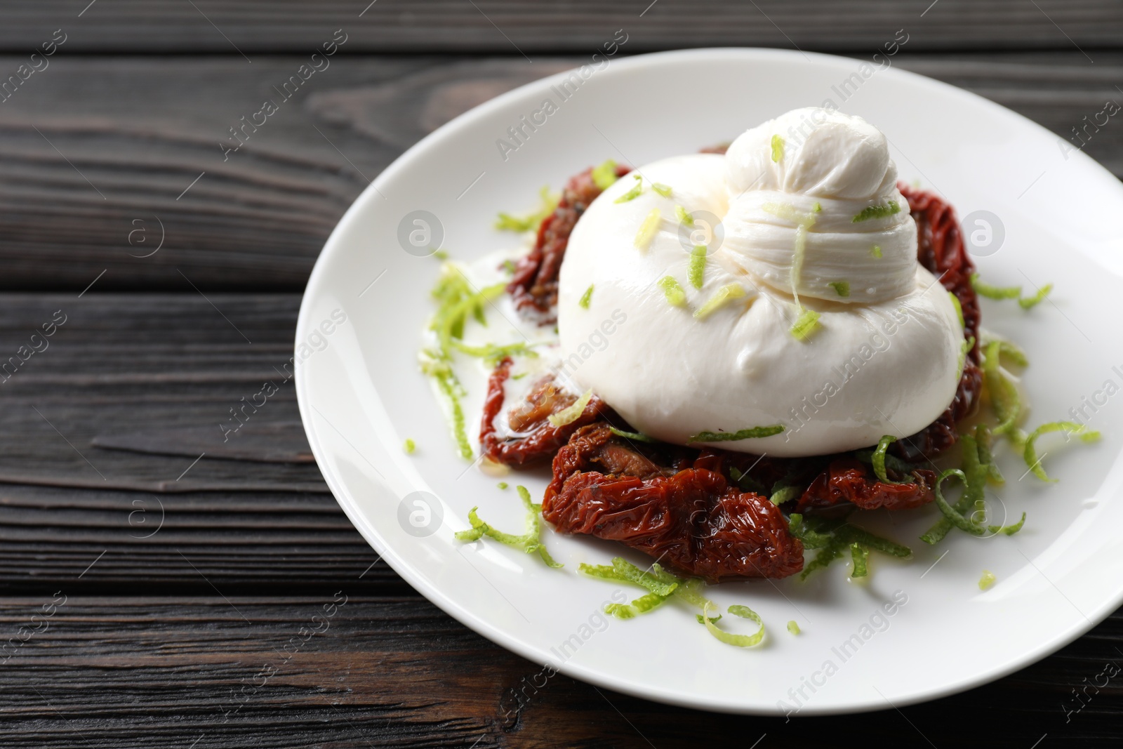 Photo of Delicious burrata cheese and sun-dried tomatoes on wooden table, closeup