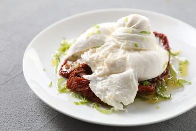 Delicious burrata cheese and sun-dried tomatoes on light grey table, closeup