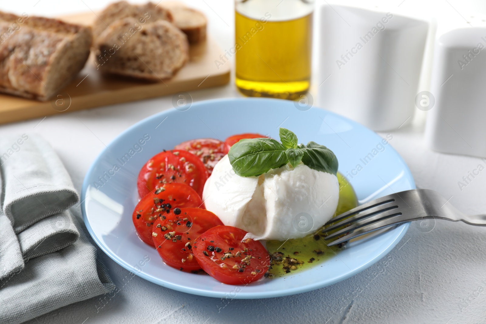 Photo of Delicious burrata cheese, tomatoes, basil and bread on white table, closeup