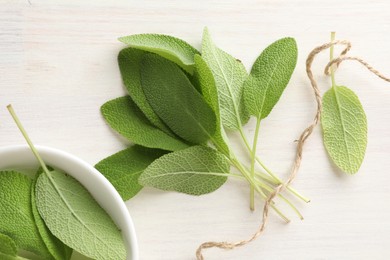 Photo of Fresh sage leaves and thread on light wooden table, top view