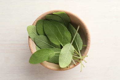 Photo of Fresh sage leaves in bowl on light wooden table, top view