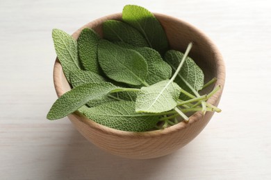 Photo of Fresh sage leaves in bowl on light wooden table, closeup