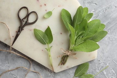 Photo of Bunch of fresh sage leaves, scissors and thread on gray textured table, flat lay