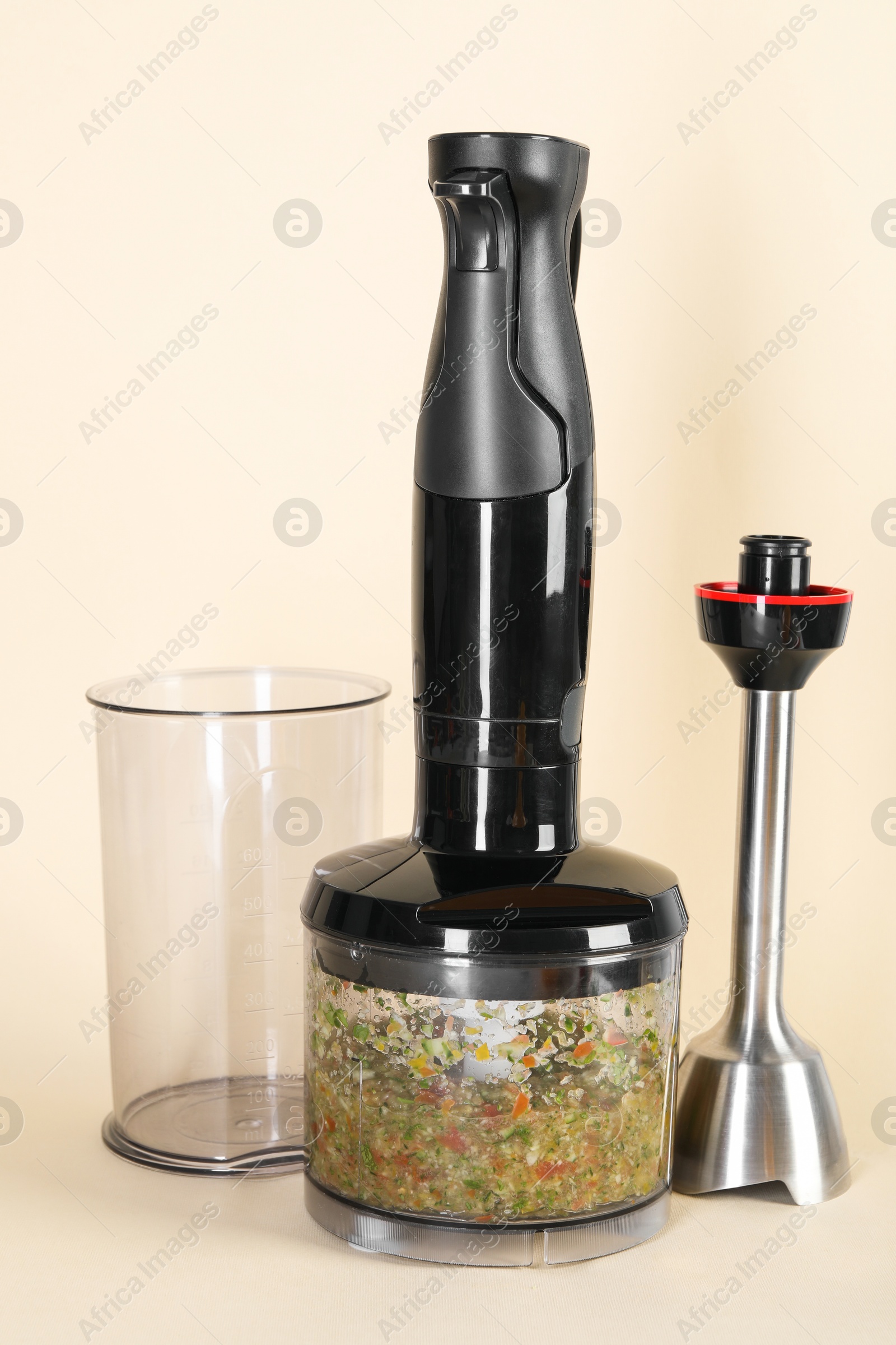 Photo of Hand blender kit and mixture of ingredients on beige background