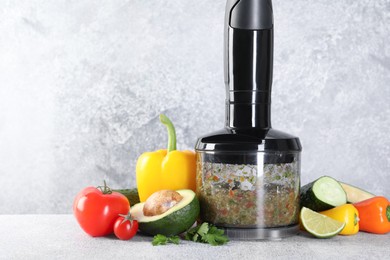 Photo of Hand blender with mixture of ingredients and fresh products on light grey table