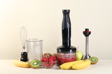 Photo of Hand blender kit, mixture of ingredients and fresh fruits on beige background