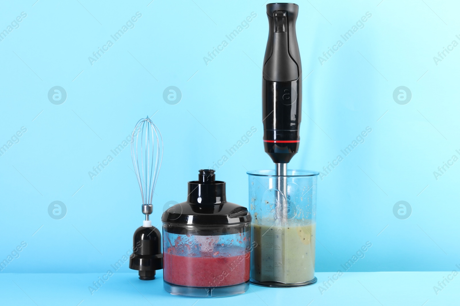 Photo of Hand blender kit and mixtures of ingredients on light blue background