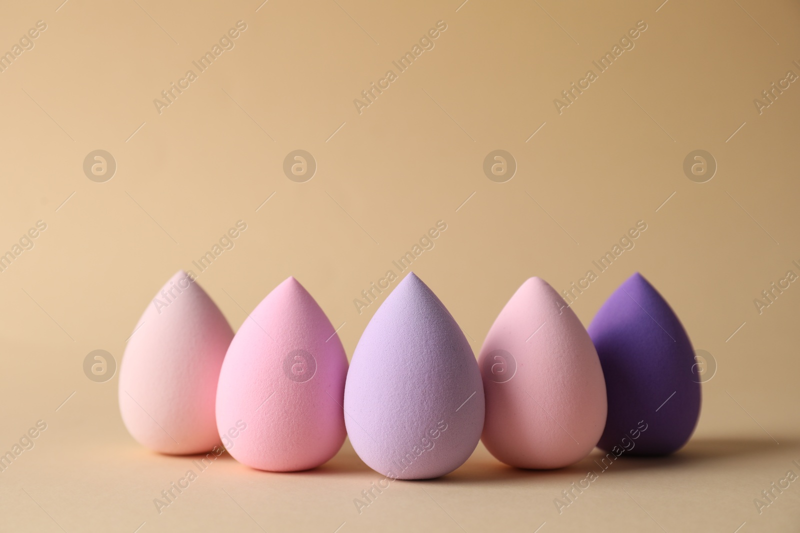 Photo of Many colorful makeup sponges on beige background. Space for text