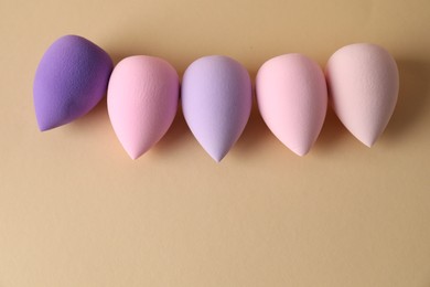 Photo of Many colorful makeup sponges on beige background, flat lay. Space for text