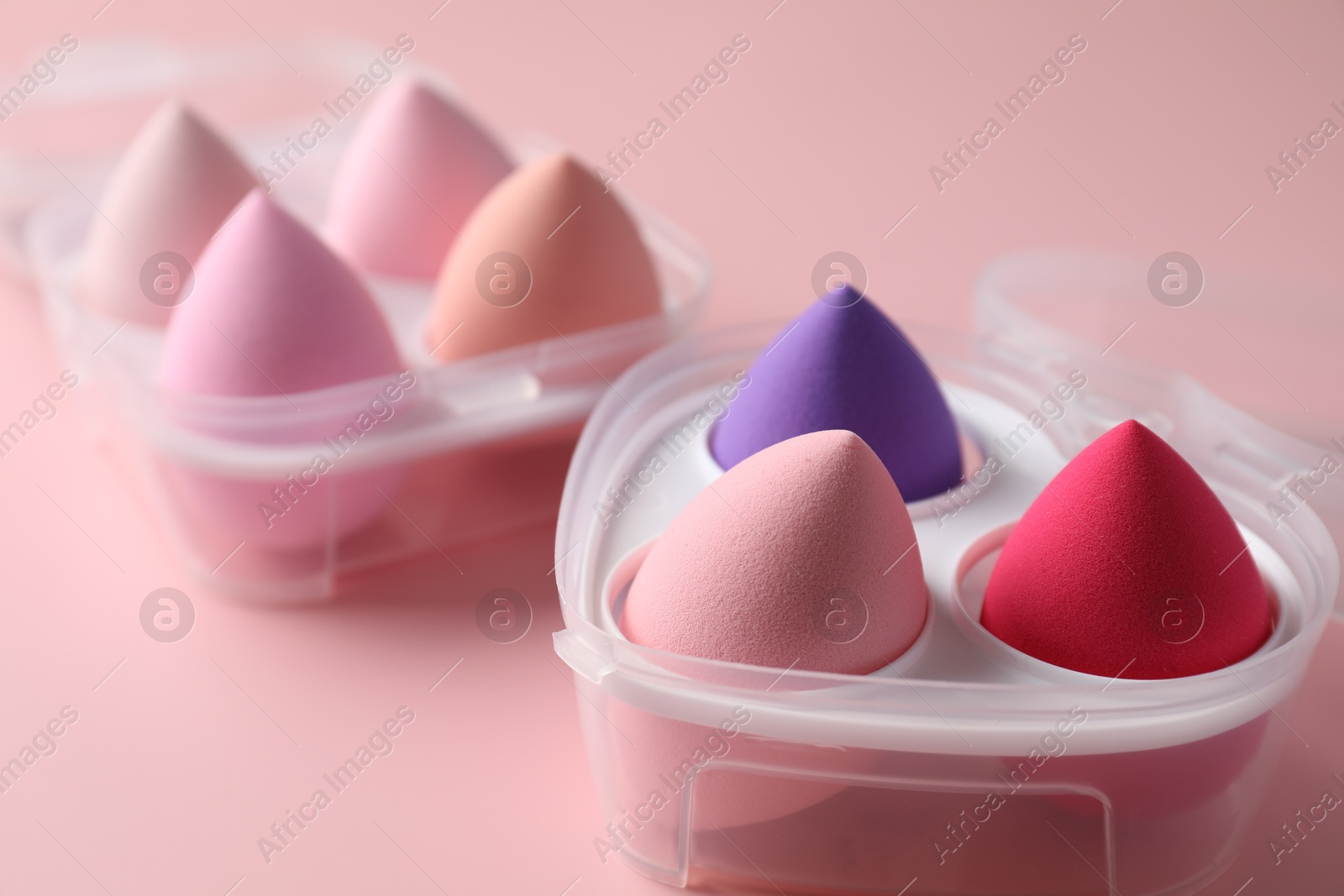 Photo of Makeup sponges in plastic containers on pink background