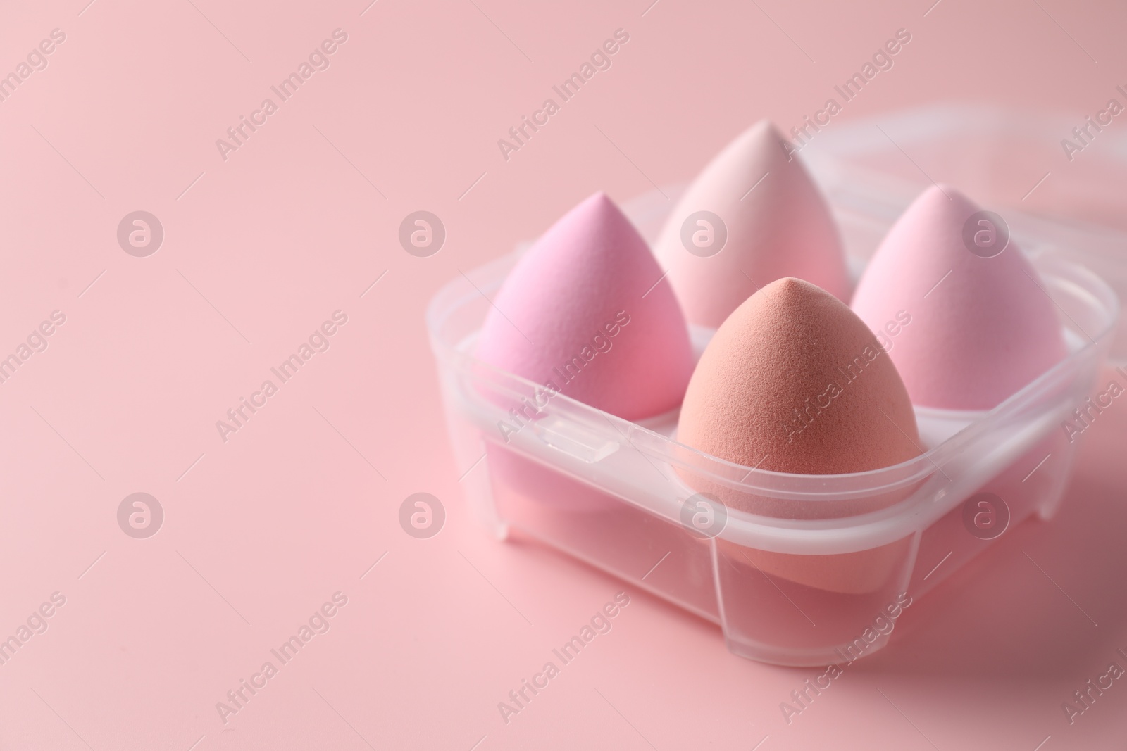 Photo of Makeup sponges in plastic container on pink background, space for text