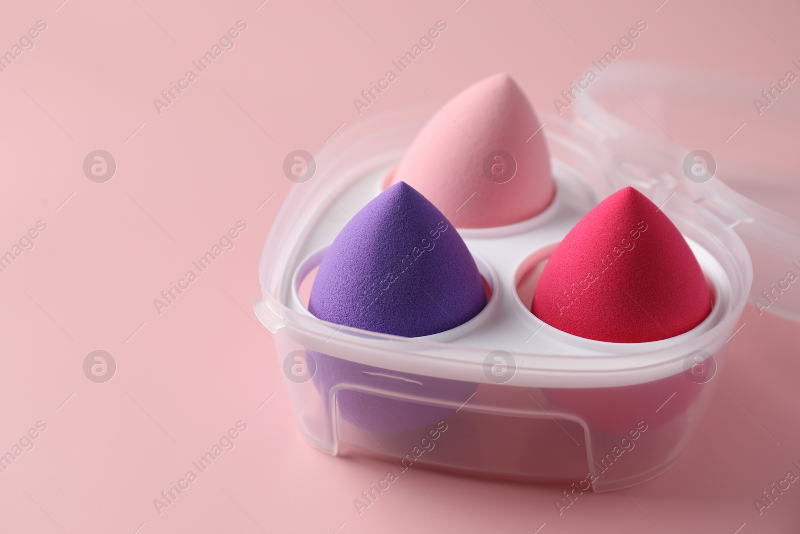 Photo of Makeup sponges in plastic container on pink background, space for text