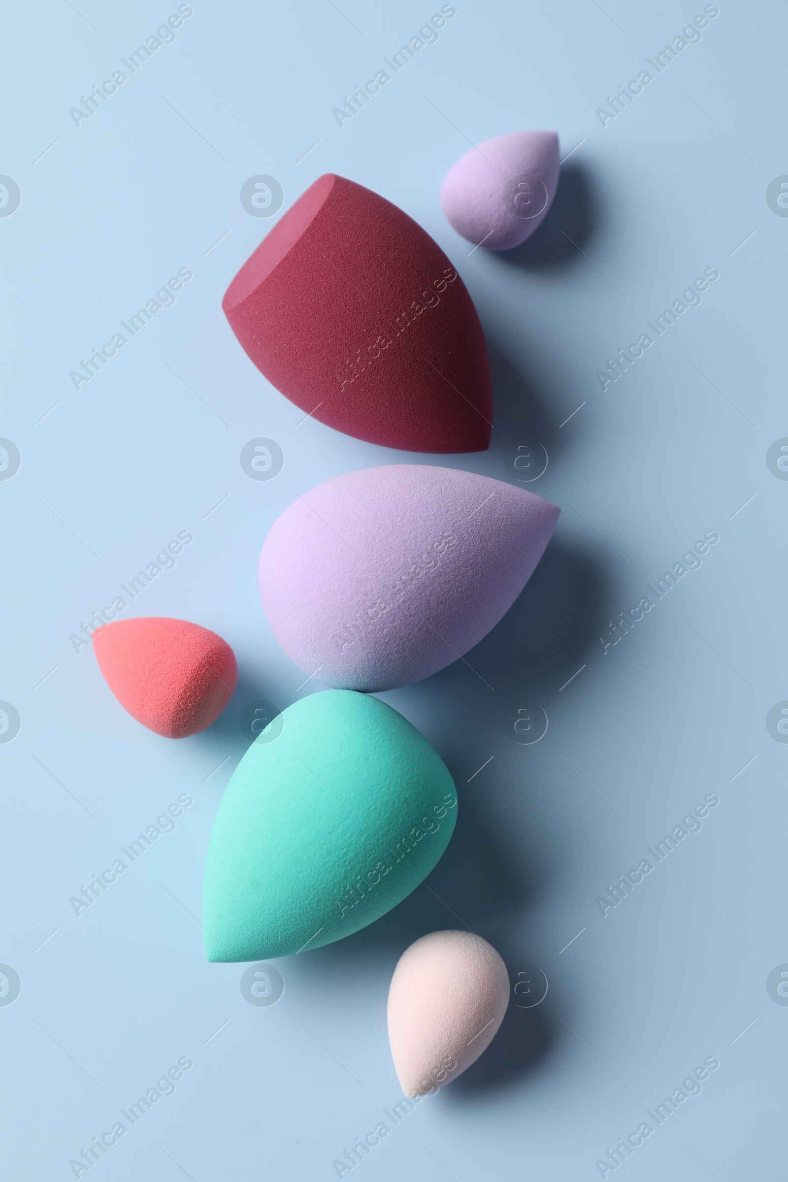 Photo of Many colorful makeup sponges on light blue background, flat lay