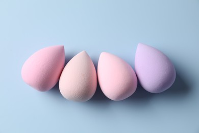 Many colorful makeup sponges on light blue background, flat lay