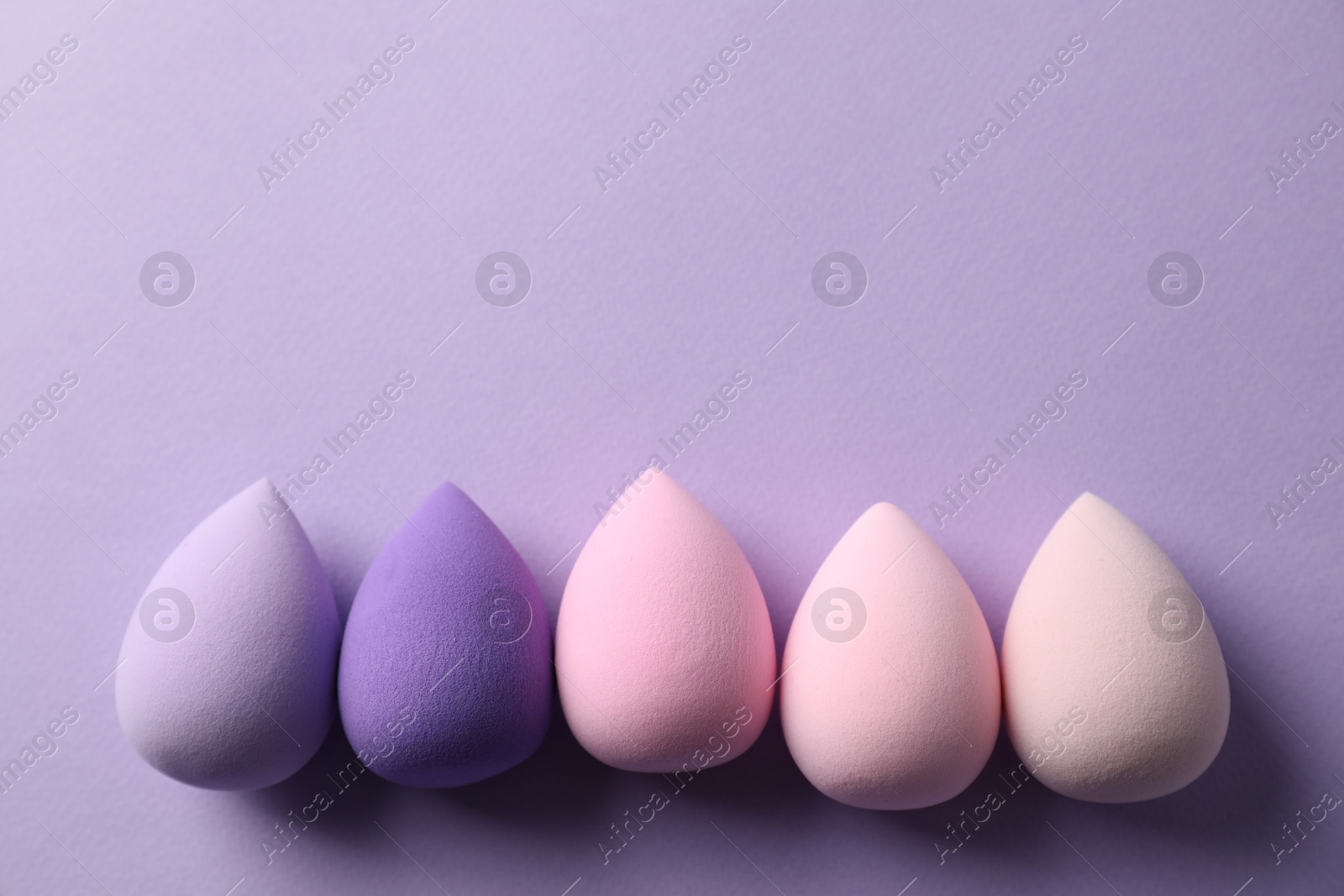 Photo of Many colorful makeup sponges on violet background, flat lay. Space for text