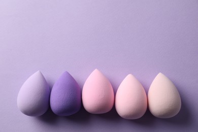 Photo of Many colorful makeup sponges on violet background, flat lay. Space for text