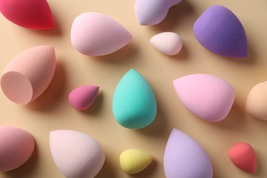 Photo of Many colorful makeup sponges on beige background, flat lay