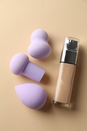 Photo of Makeup sponges and skin foundation on beige background, flat lay