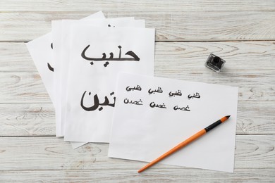 Calligraphy. Papers with words Milk and Antelope in Arabian language, inkwell and brush on white wooden table, flat lay