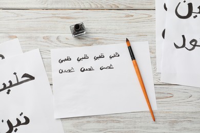 Photo of Calligraphy. Papers with words Fig, Milk, Doctor in Arabian language, inkwell and brush on white wooden table, flat lay