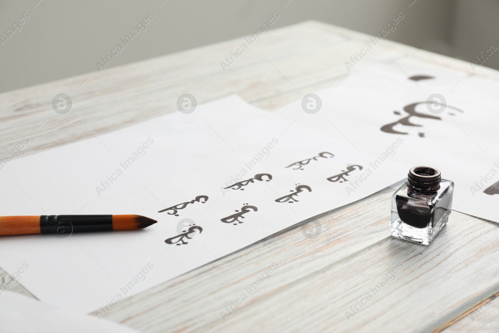 Photo of Calligraphy. Papers with written word Branch in Arabian language, inkwell and brush on white wooden table, closeup