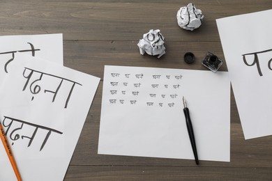 Calligraphy. Papers with words Reading and Read in Hindi, inkwell, fountain pen and brush on wooden table, flat lay