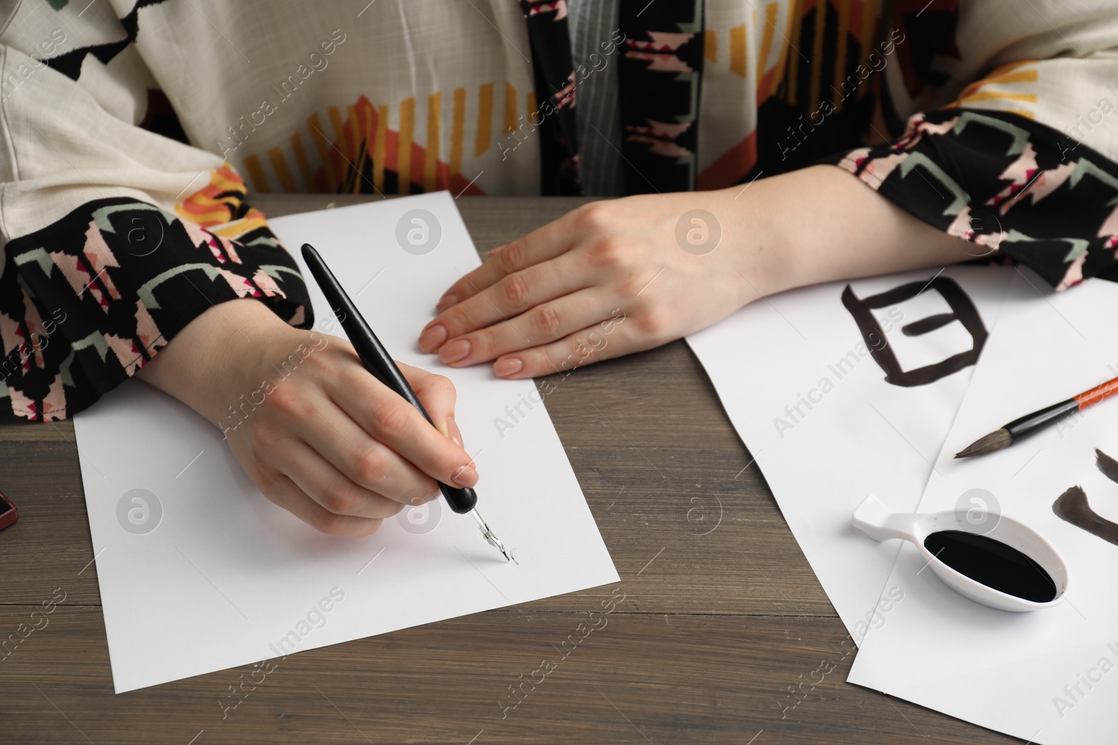 Photo of Calligraphy. Woman with fountain pen writing at wooden table, closeup. Word Speak in Chinese on paper