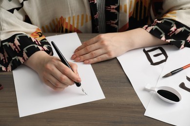 Calligraphy. Woman with fountain pen writing at wooden table, closeup. Word Speak in Chinese on paper