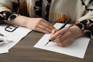 Photo of Calligraphy. Woman with fountain pen writing at wooden table, closeup. Word Speak in Chinese on paper