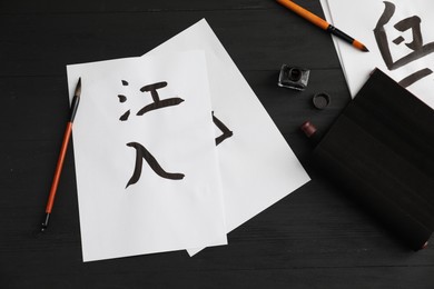 Calligraphy. Flat lay composition with written words River and Entrance in Chinese and inkwell on black wooden table