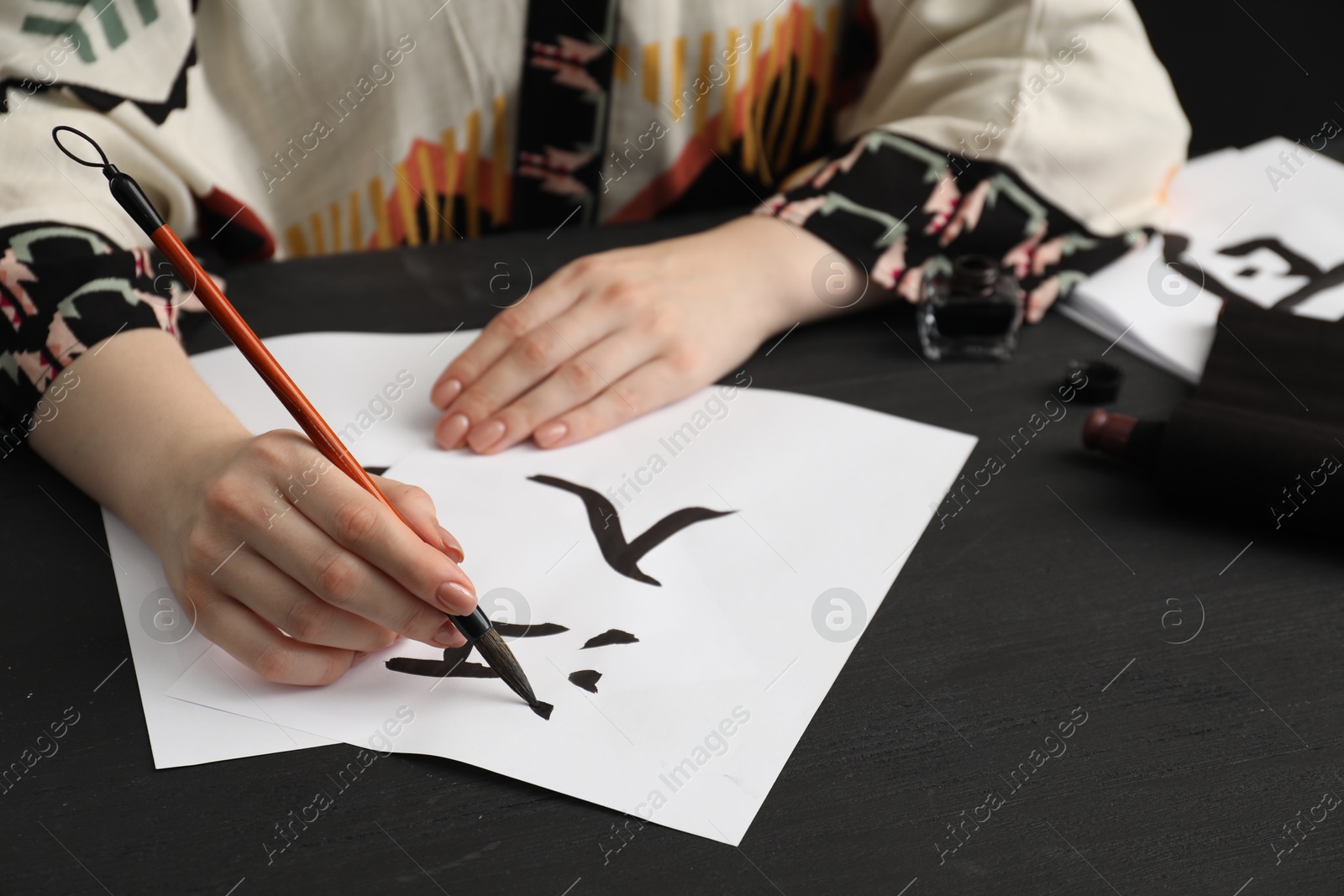 Photo of Calligraphy. Woman with brush writing words River and Entrance in Chinese on paper at black wooden table, closeup