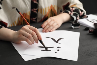 Calligraphy. Woman with brush writing words River and Entrance in Chinese on paper at black wooden table, closeup