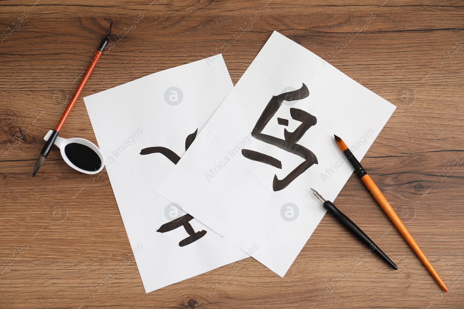 Photo of Calligraphy. Papers with written words Bird, River and Entrance in Chinese, inkwell, fountain pen and brushes on wooden table, flat lay