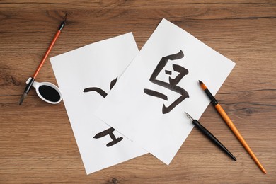 Calligraphy. Papers with written words Bird, River and Entrance in Chinese, inkwell, fountain pen and brushes on wooden table, flat lay