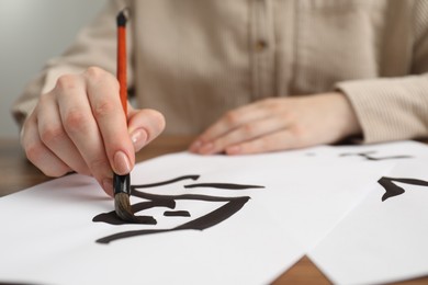 Photo of Calligraphy. Woman with brush writing word Bird in Chinese on paper at table, closeup