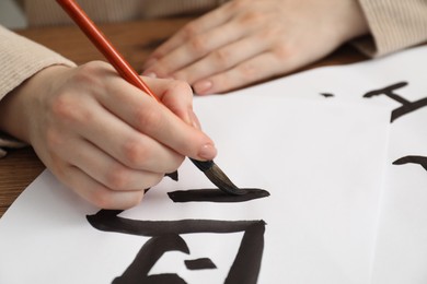 Photo of Calligraphy. Woman with brush writing word Bird in Chinese on paper at table, closeup