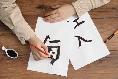 Calligraphy. Woman with brush and inkwell writing words Bird, River and Entrance in Chinese on paper at wooden table, top view