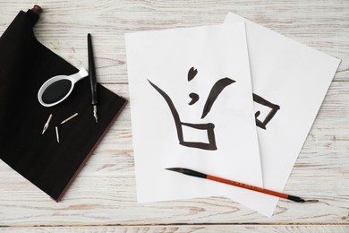 Calligraphy. Papers with written word Finish in Chinese, inkwell, fountain pen and brush on white wooden table, flat lay