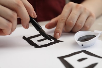 Photo of Calligraphy. Woman with brush and inkwell writing words Speak and Day in Chinese on paper at table, closeup