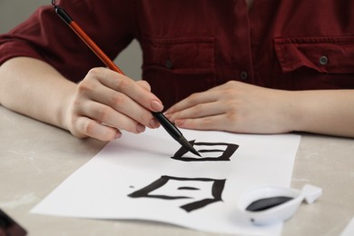 Calligraphy. Woman with brush and inkwell writing words Speak and Day in Chinese on paper at light marble table, closeup