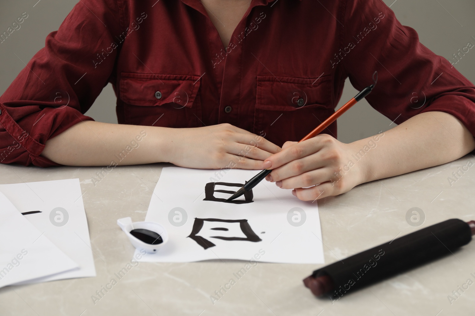 Photo of Calligraphy. Woman with brush and inkwell writing words Speak and Day in Chinese on paper at light marble table, closeup