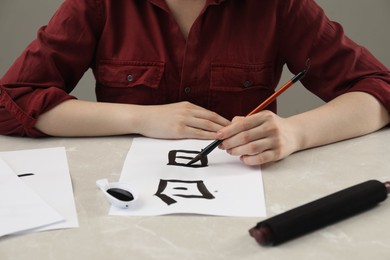 Calligraphy. Woman with brush and inkwell writing words Speak and Day in Chinese on paper at light marble table, closeup