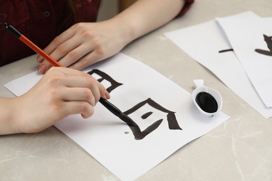 Photo of Calligraphy. Woman with brush and inkwell writing words Speak and Day in Chinese on paper at light marble table, closeup