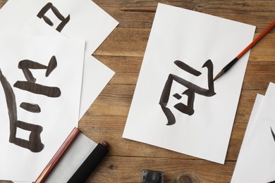 Photo of Calligraphy. Papers with written Chinese hieroglyphs, inkwell and brush on wooden table, flat lay