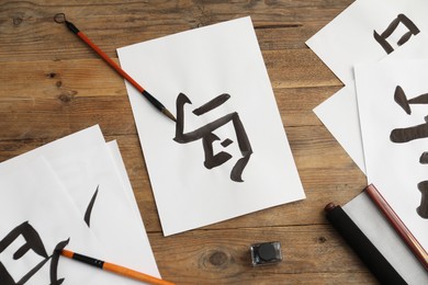 Calligraphy. Papers with written Chinese hieroglyphs and brushes on wooden table, flat lay