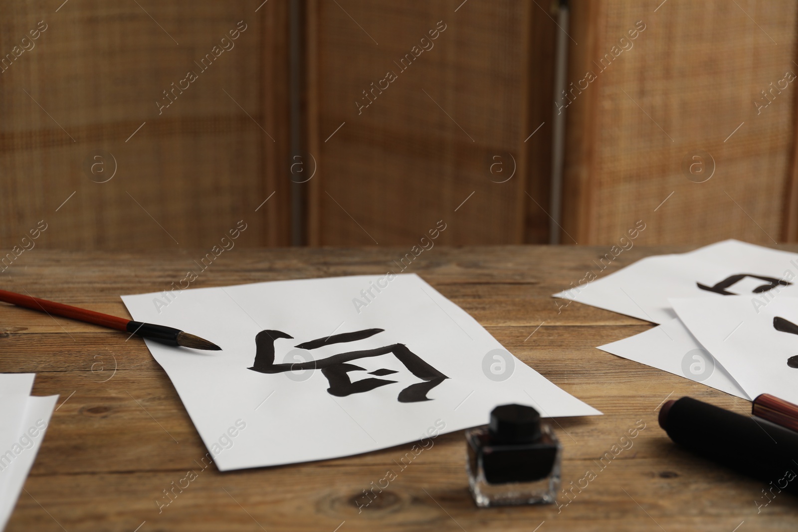 Photo of Calligraphy. Papers with written Chinese hieroglyphs, inkwell and brush on wooden table