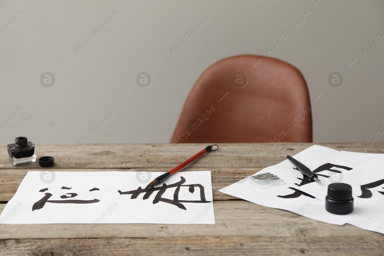 Photo of Calligraphy. Papers with written Chinese hieroglyphs, inkwell, fountain pen and brush on wooden table