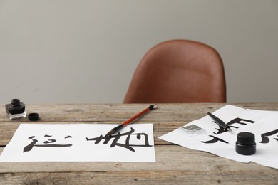 Photo of Calligraphy. Papers with written Chinese hieroglyphs, inkwell, fountain pen and brush on wooden table